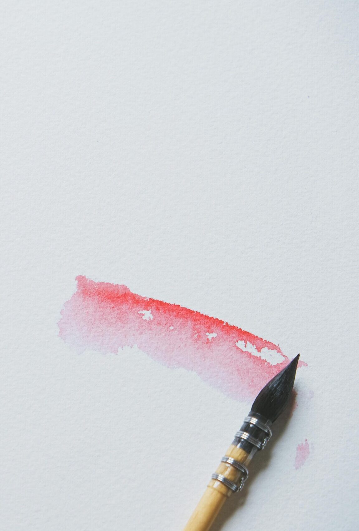 Close-up of red watercolor strokes and a brush on white canvas, showcasing artistic creativity.